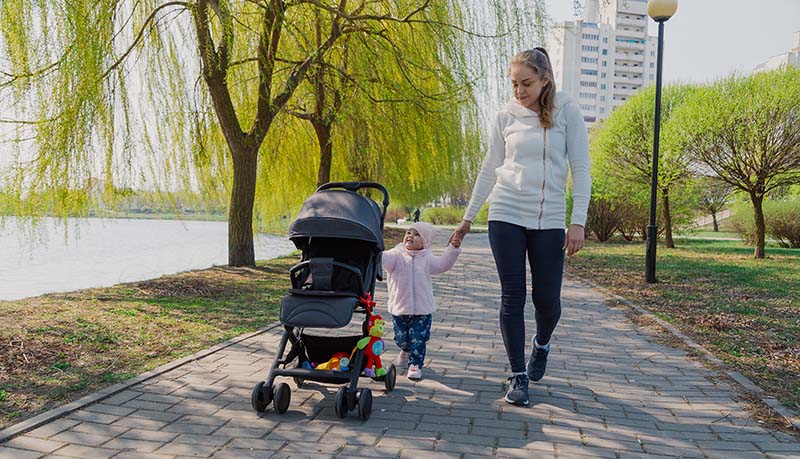 a young mother walks with a child who rolls a pram.